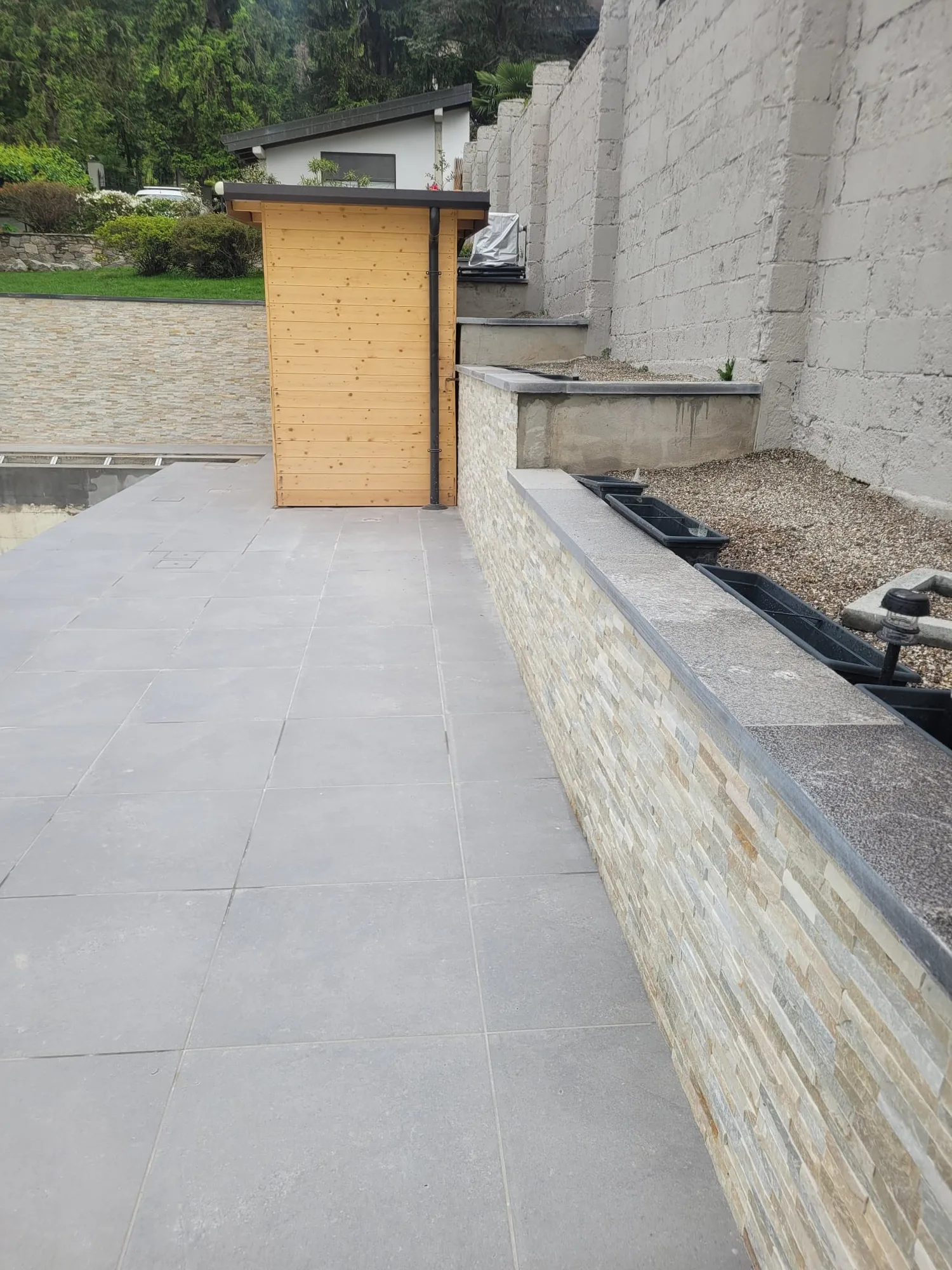 Bordo piscina pavimentato con il muretto in pietra finito e la casetta in legno sullo sfondo
