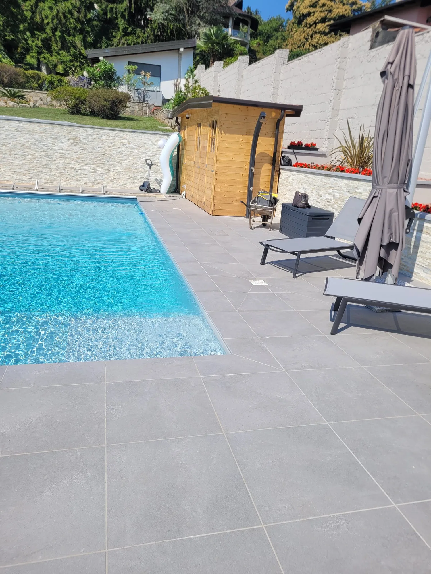 Bordo piscina finito: pavimento in gres grigio, lettini e casetta in legno costruita sul posto