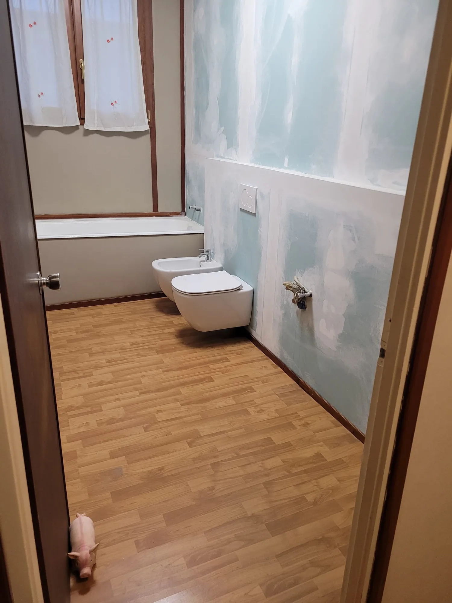 Bagno in fase di finitura: pavimento effetto legno posato, sanitari sospesi montati, pareti da tinteggiare
