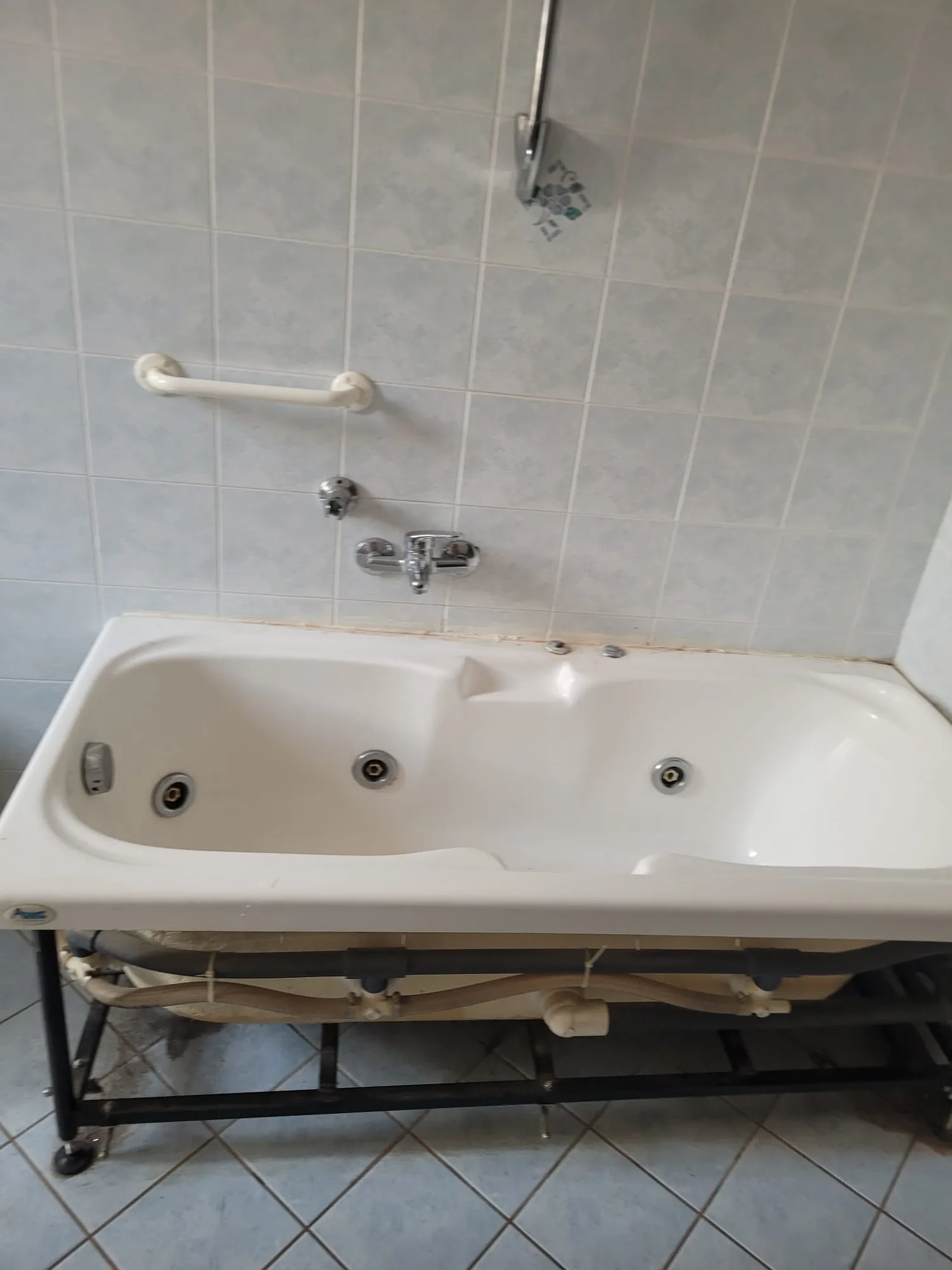 Bagno prima dei lavori: vecchia vasca idromassaggio scoperta sul telaio, piastrelle celesti