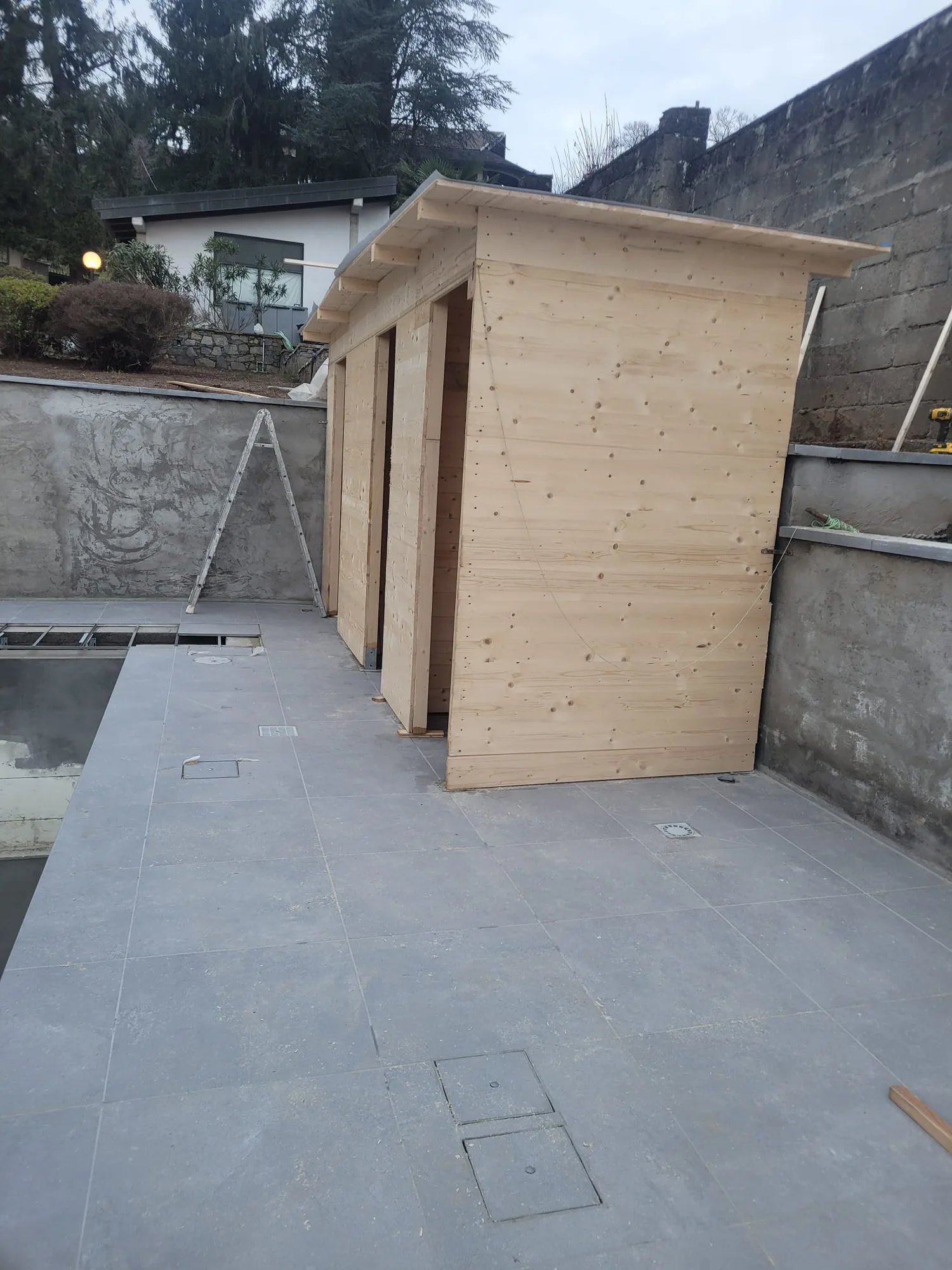 Casetta in legno grezzo in fase di montaggio a bordo piscina, pavimento in gres già posato
