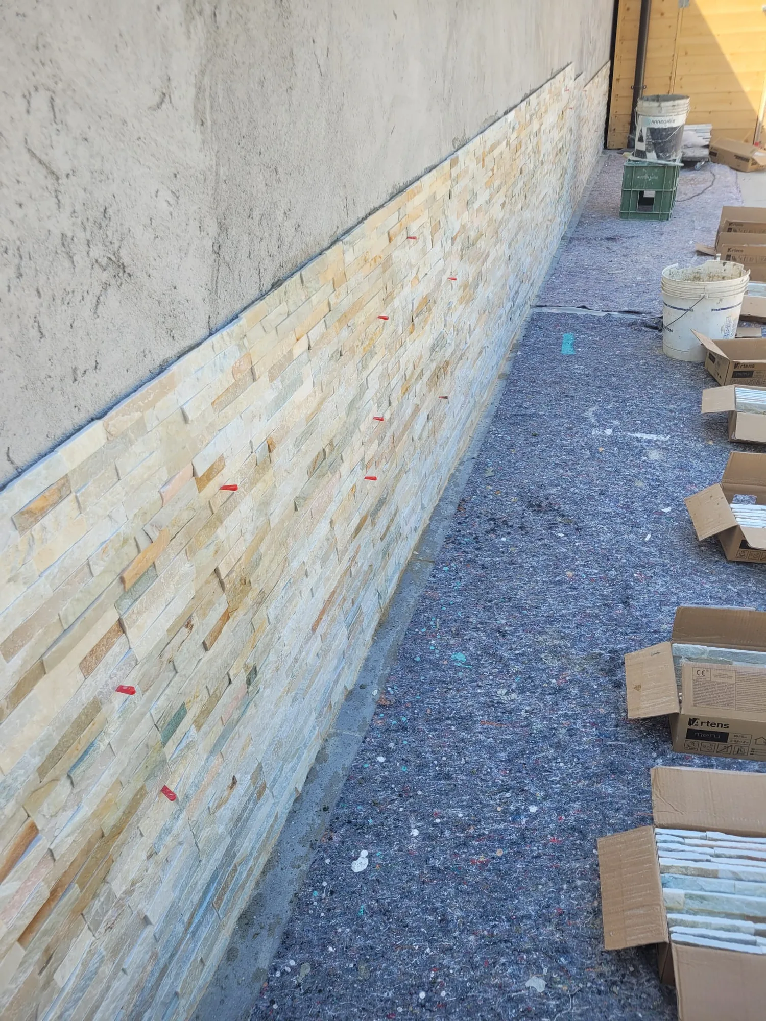 Rivestimento in pietra a spacco in corso di posa sul muretto perimetrale, scatole di materiale a terra